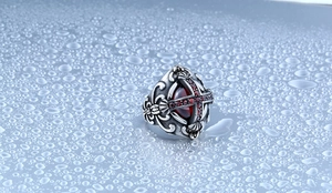 Gros plan sur une bague vintage en acier avec pierre rouge et motif de croix gothique