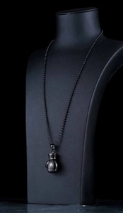 Detail of matte black boxing glove pendant necklace on a black jewelry neck bust