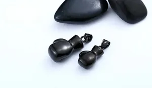 Detail view of black polished stainless steel boxing glove pendants on dark river stones