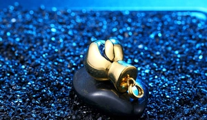 Polished golden boxing glove pendant displayed on a smooth dark stone with blue crystals