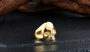 Makroaufnahme eines polierten Gold-Totenkopfrings mit Relief auf dunklem Stein