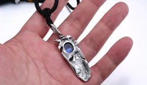 Macro detail of vintage feather pendant with blue gemstone and black woven cord necklace