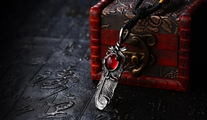 Macro shot of retro feather pendant with red gemstone and detailed brushed metal texture