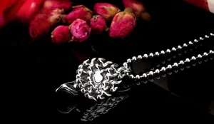 Macro shot of silver flame textured round pendant on bead chain over black reflection