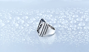 Macro shot of square silver signet ring with lightning bolt engraving on water droplets