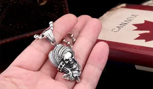 Macro shot of silver skull pendant with detailed feather headpiece held by hand