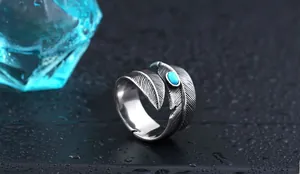 Macro shot of turquoise inlaid feather ring on textured surface with water droplets