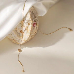Elegant gold rose tassel Y-necklace featuring floral charms on a white stone background