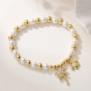 Detailed view of pearl bracelet with crystal coconut tree and turtle charms on fabric