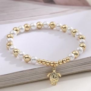 Minimalist pearl bracelet with a golden sea turtle pendant on a decorative open book