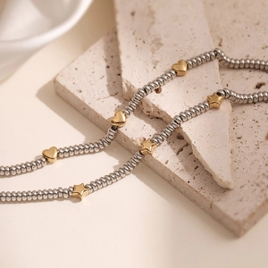 Minimalist silver beaded bracelet with gold heart and star charms on stone background