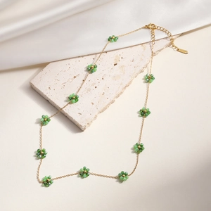 Elegant gold necklace with green beaded flowers on a textured stone and silk background