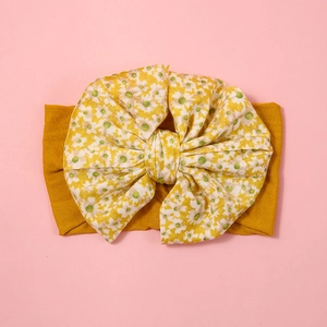 Detail of soft mustard yellow nylon baby headband with a large floral bow decoration