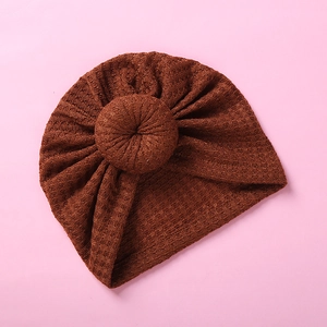Detailed close-up showing the waffle knit texture and top knot of the caramel baby hat