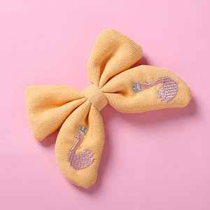 Détail du nœud à cheveux en tricot jaune avec broderie cygne rose et petite couronne argentée