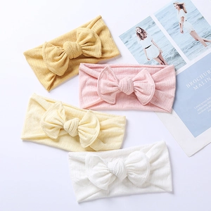 Set of four knitted baby headbands with large bows in yellow, pink, beige, and white
