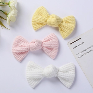 Close-up of three knitted waffle fabric bow hair clips in yellow, pink and white colors