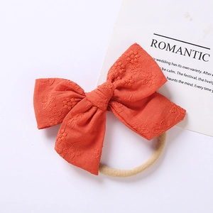 Dettaglio di fiocco in cotone ricamato arancione su fascia elastica in nylon per bimbi
