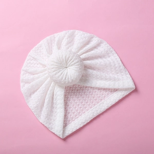 Detailed close-up of white waffle knit baby turban hat with donut knot on pink backdrop
