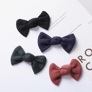 Close-up of four knitted bow hair clips in black, navy, grey, and brick red on a card