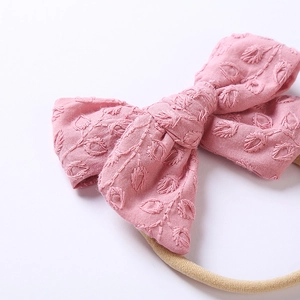Dettaglio macro della fascia con fiocco in cotone rosa e ricamo a foglia per neonati