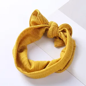 Bright yellow ribbed knit baby headband featuring a large bow on a white background
