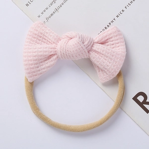 Detail of pink waffle knit baby headband with elastic nylon loop and soft bow texture