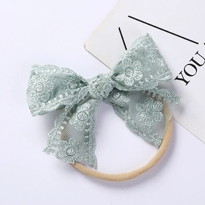 Close-up of mint green lace bow baby headband with floral embroidery and soft nylon strap