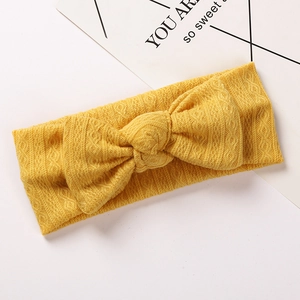 Détail d'un bandeau tricoté jaune pour bébé avec grand nœud et motifs texturés