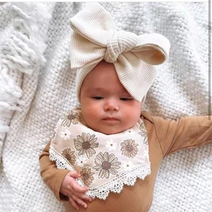 Detail of baby waffle bow headband and sunflower floral bib on soft white knit blanket