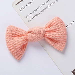 Close-up of a pink knitted bow hair clip featuring a waffle texture on a display card