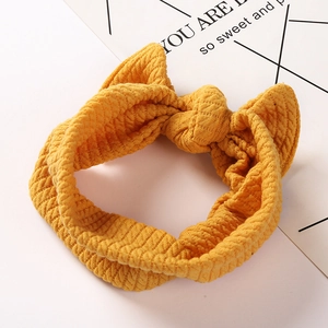 Detail of ginger yellow waffle knit baby headband with a large bow on white pedestal