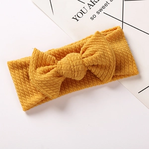 Detailed close-up of ginger yellow ribbed knit baby headband with a large bow