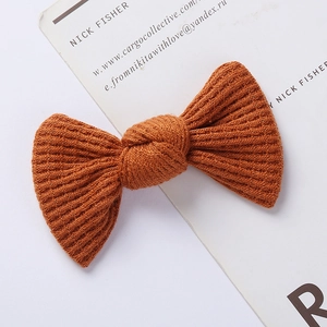 Close-up of a caramel-colored knitted bow hair clip showing textured waffle knit fabric