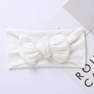 Detail view of a white knitted baby headband featuring a large bow and ribbed texture