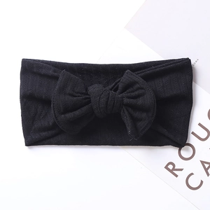 Detail view of black ribbed knit baby headband with a large bow on white background