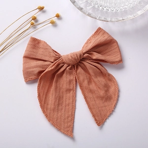 Detail view of brick red jacquard cotton bow clip showing vertical fabric texture and frayed edges