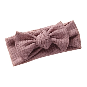 Pink knit baby headband featuring large bow and honeycomb texture on white background