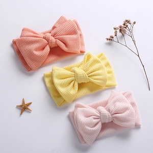 Detailed waffle texture on three-piece baby bow headband set in orange and soft pink