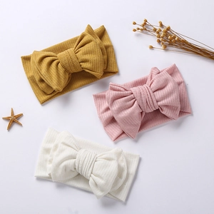 Three soft ribbed knit baby headbands with oversized double-layered bows in warm colors