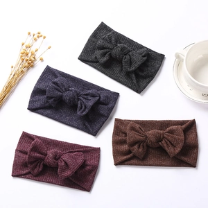Detail of four ribbed knit baby headbands with large bows in dark colors on white surface