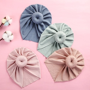 Flat lay of four ribbed knit baby turban hats with donut knots on a pink background