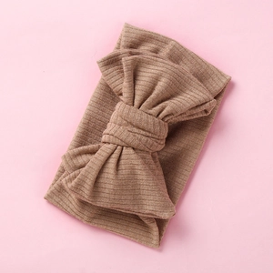 Detailed texture of light brown ribbed knit fabric with a large oversized bow on headband