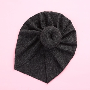 Detail of dark grey ribbed knit baby turban featuring a decorative donut knot on light pink background