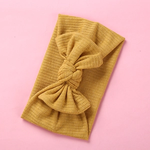 Ginger yellow ribbed knit baby headband with a large elastic bow on pink background