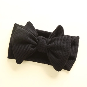 Detail of black waffle knit baby headband featuring a large double layered bow texture