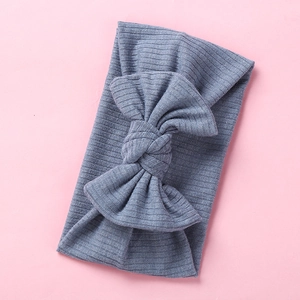 Detail of blue ribbed knit baby headband featuring a large elastic bow on pink background