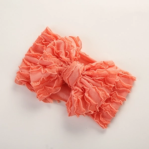Gros plan du bandeau bébé en tissu côtelé rose corail avec un grand nœud à volants