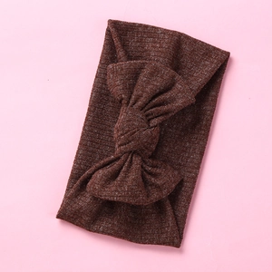 Close-up of dark brown ribbed knit baby headband with a large bow on pink background