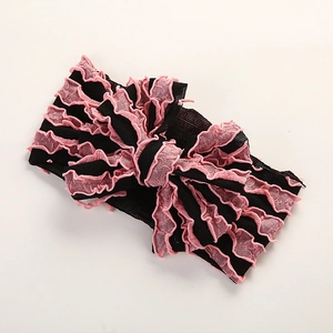 Détail d'un bandeau pour bébé fait main avec un nœud rose à volants et une bande noire